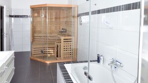A modern bathroom with a glass-enclosed sauna, a large bathtub, and a white tiled shower area. - Central Sauna & Loft Apartments Leipzig (Leipzig)