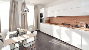 A modern kitchen with white cabinets, a wooden countertop, and a dining area with a glass table and chairs. - Central Sauna & Loft Apartments Leipzig (Leipzig)