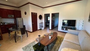 A living room with a sofa, a coffee table, and a TV. There is a dining area with chairs and a table.