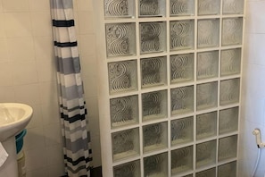 Een badkamer met een wit wastafelmeubel, een douchegordijn met strepen en een betegelde muur met een geometrisch patroon.