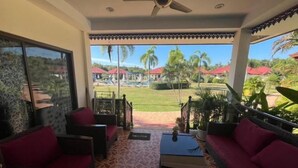 A covered outdoor seating area with wicker furniture and a view of a pool and palm trees.
