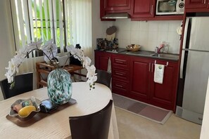 Een keuken met rode kastjes, een magnetron en een koelkast. Op de eettafel staat een vaas met bloemen.