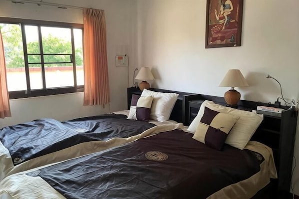 Habitación de hotel con dos camas, una ventana con cortinas, un cuadro en la pared y dos lámparas de noche.