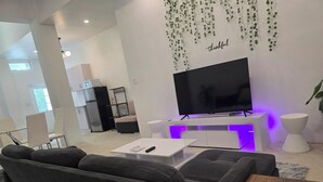 Ein modernes Wohnzimmer mit großem Flachbildfernseher, einer Couch, einem Couchtisch und einem kleinen Holznachttisch.