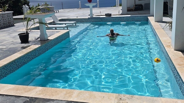 Ein Swimmingpool mit Blick auf den Ozean, umgeben von einem weißen Gebäude mit einem Balkon.
