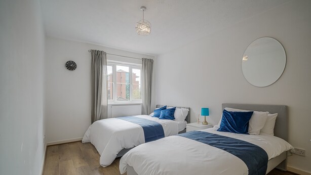 A bedroom with two beds, a window with curtains, a round mirror, and a clock on the wall.