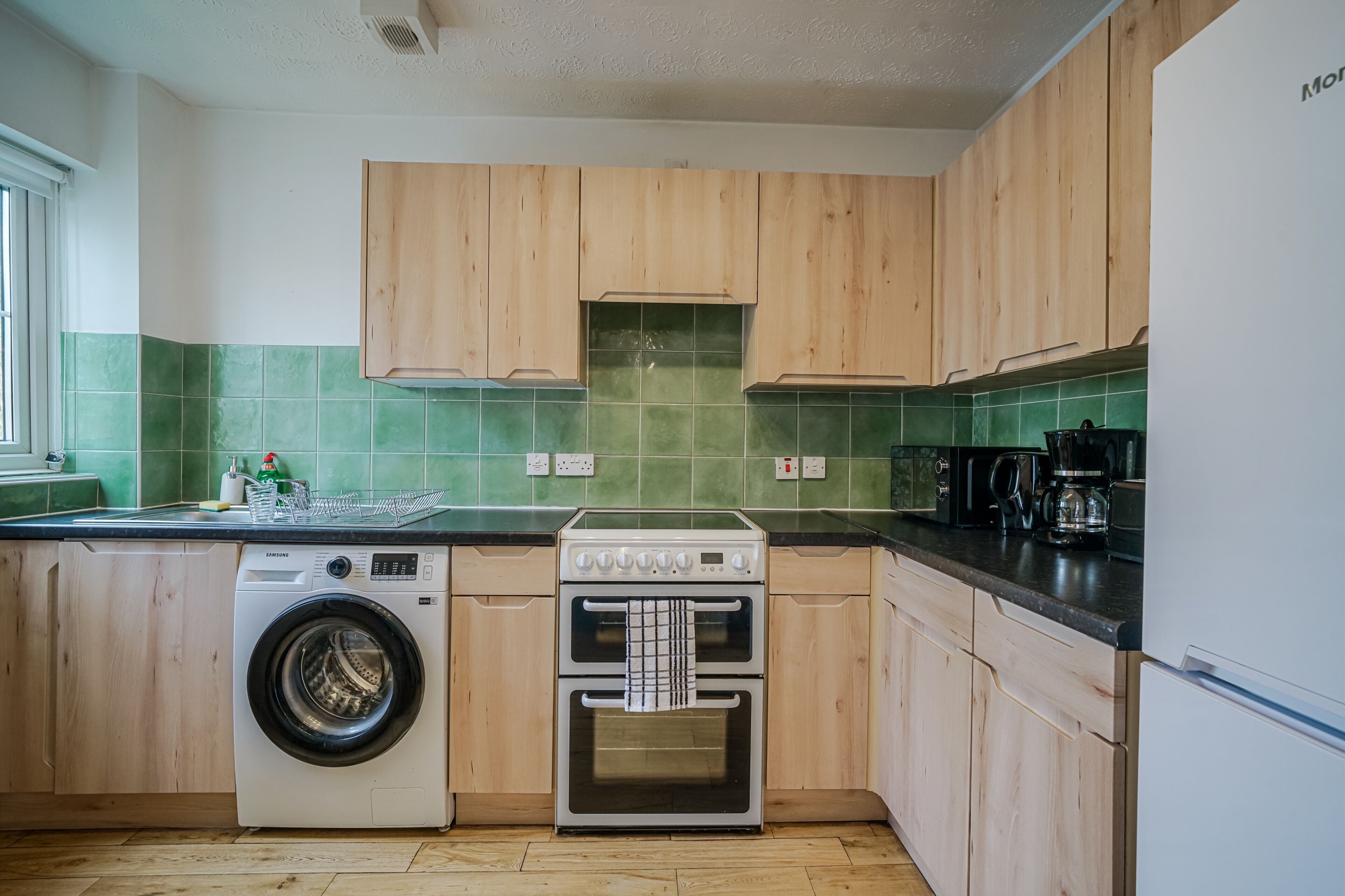 A kitchen with wooden cabinets, a washing machine, an oven, and a coffee maker.