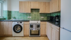 A kitchen with wooden cabinets, a washing machine, an oven, and a coffee maker.