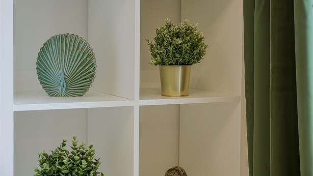A white shelf with a green decorative plate, a gold pot with green foliage, and a small green plant. - Salford City Escape - Modern 2 Bedroom Apartment (Salford)