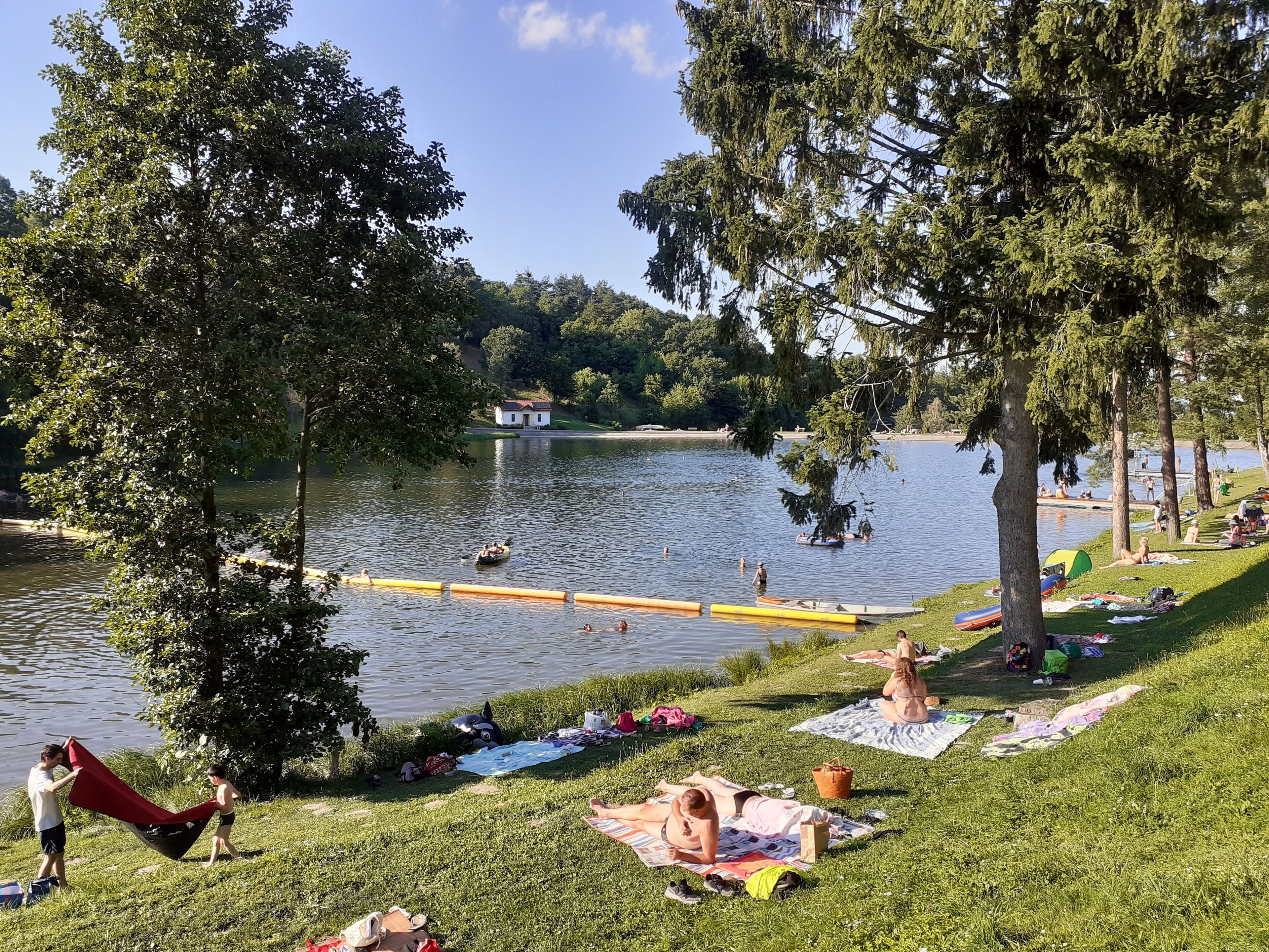 Ein Park am Seeufer mit Picknickplätzen, einem Steg und Menschen bei verschiedenen Aktivitäten.