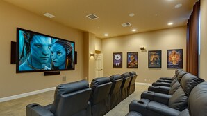 Une salle de cinéma privée équipée d’un grand téléviseur à écran plat, de plusieurs rangées de fauteuils inclinables en cuir et d’un sol recouvert de moquette.