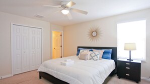 Une chambre à coucher avec un lit, un ventilateur de plafond, une table de chevet, une lampe et une porte.
