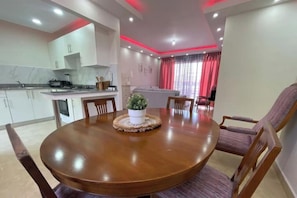 Uma sala de jantar moderna com uma mesa redonda de madeira, rodeada por cadeiras, e uma pequena planta em vaso no centro.