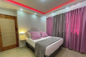 Quarto com cama, mesa de cabeceira, luminária na parede e uma porta.