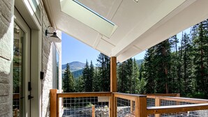 Eine Holzterrasse mit Dachfenster, einer Steinmauer und Blick auf einen Wald und Berge.