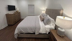 Un dormitorio con cama, cómoda, televisor, ventilador de techo y ventana con persianas.
