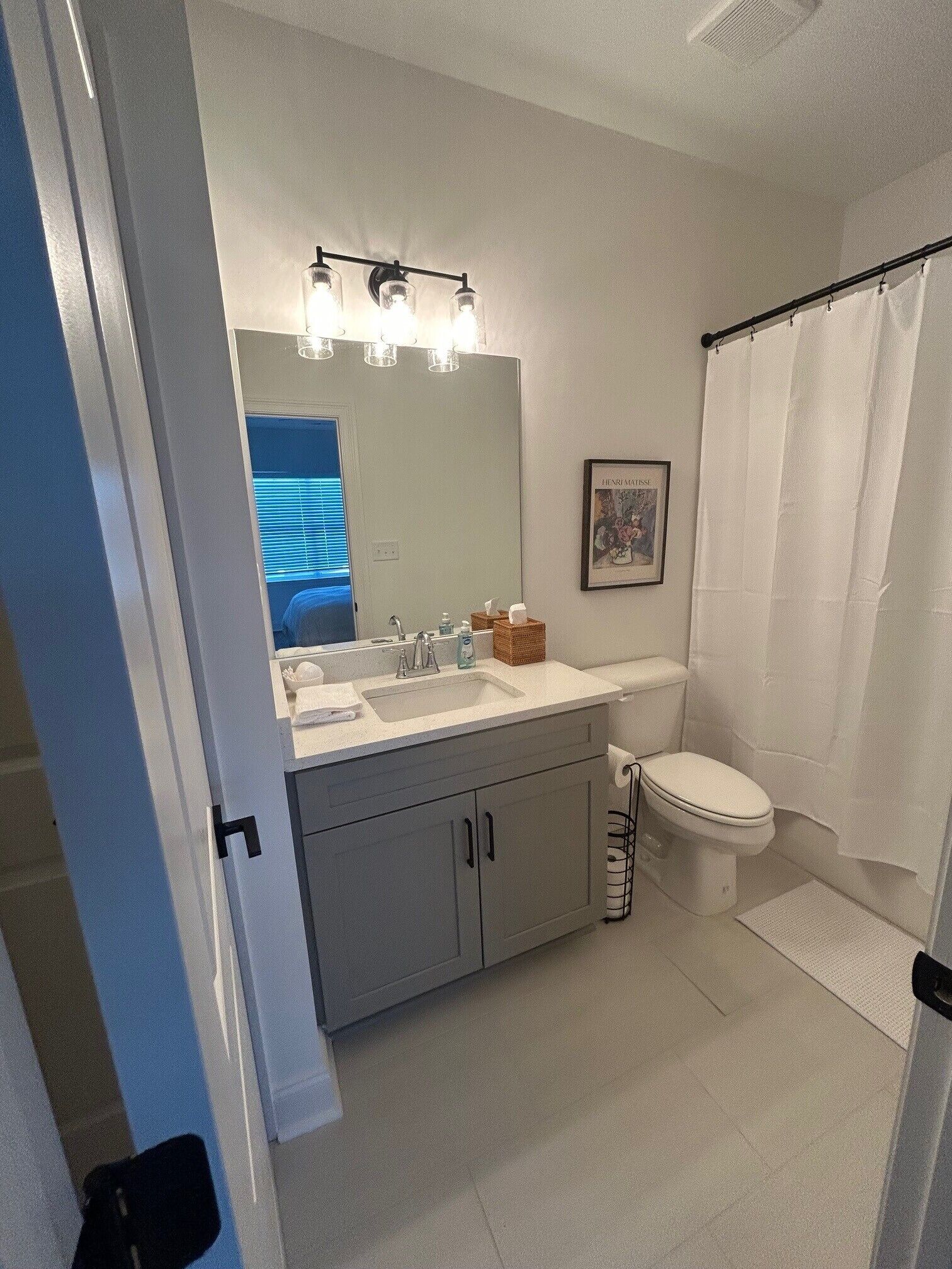 A bathroom with a white sink, mirror, and toilet. There is a shower curtain and a framed picture on the wall.
