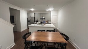 Una cocina moderna con armarios blancos, una isla central y una zona de comedor con mesa y sillas de madera.