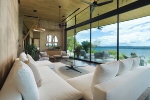 Ein modernes Wohnzimmer mit großem Fenster, weißen Sofas und einem Essbereich mit Stühlen und Tisch.