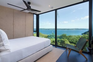 A modern bedroom with a large window, a bed, a chair, and a ceiling fan. - Villa Coral: 5BR Oceanfront Papagayo Estate, Private Pool, Golf & Beach Clubs! (Peninsula Papagayo)