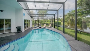 Une piscine intérieure moderne avec des parois en verre transparent, un design incurvé et une vue sur les palmiers et la végétation environnante.