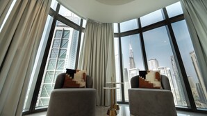 Ein modernes Zimmer mit zwei grauen Sesseln, einem kleinen runden Tisch und Blick auf eine Stadtlandschaft durch große Fenster.