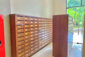 Eine Reihe brauner Briefkästen mit Beschriftungen, ein roter Schrank und ein Fenster mit Blick ins Grüne.