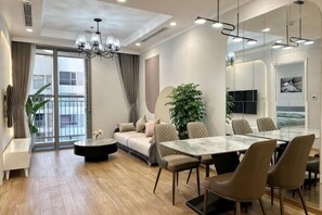 A modern living room with a sofa, dining table, chairs, a coffee table, and a large plant. - HaLa Housing - Vinhomes D'capitale Apartment Hanoi (Hanoi)