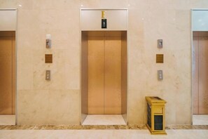 Drie liftdeuren met een marmeren vloer en een klein houten doos ernaast.