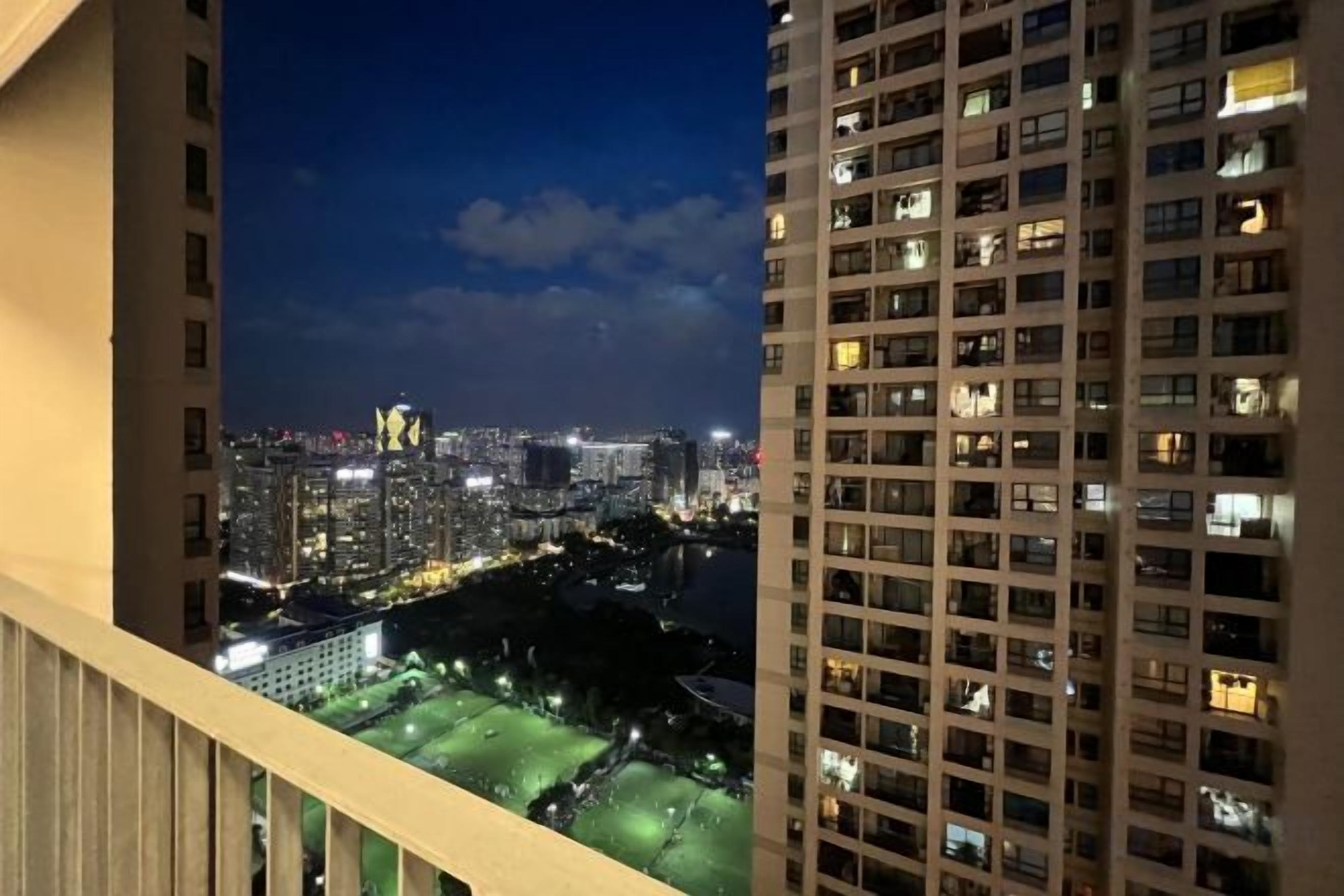 A high-rise building with multiple floors, a balcony, and a view of a cityscape at night.