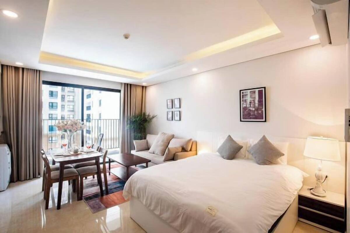 Una habitación de hotel moderna con una cama grande, una zona de comedor y un balcón con cortinas.