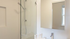 Uma casa de banho moderna com chuveiro em cabine de vidro, um espelho grande e lavatório com artigos de higiene pessoal.