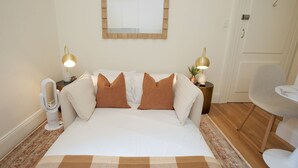 Quarto arrumado com uma cama, duas mesas de cabeceira com abajures, uma cadeira e uma pequena mesa.