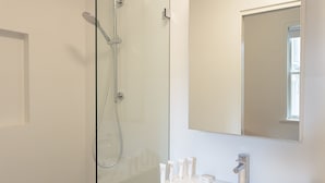 Uma casa de banho moderna com chuveiro em cabine de vidro, um espelho grande e lavatório com artigos de higiene pessoal.