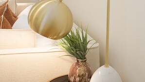 Um quarto com um sofá bege, um vaso branco com plantas verdes e duas luminárias pendentes.