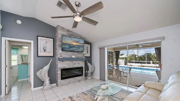 A modern living room with a fireplace, a ceiling fan, and a view of a swimming pool. - Beautiful 3-bedroom Pool home on Canal in wonderful Rotonda West, Close to Beach (Rotonda West)