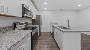 A modern kitchen with white cabinetry, a granite countertop, stainless steel appliances, and a wooden floor. - Unwind in this stylish, newly renovated 1-bedroom suite near Topaz Lake. (Gardnerville)