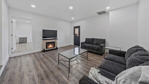 A modern living room with a fireplace, a flat-screen TV, and a gray sofa. - Unwind in this stylish, newly renovated 1-bedroom suite near Topaz Lake. (Gardnerville)