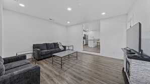 A modern living room with a grey sofa, a glass coffee table, and a flat-screen TV on a stone-textured stand. - Unwind in this stylish, newly renovated 1-bedroom suite near Topaz Lake. (Gardnerville)