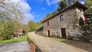 Un edificio de piedra con puerta roja y ventana, rodeado de árboles y un camino adoquinado.