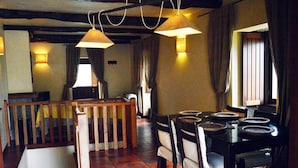 Un comedor con una mesa y sillas de madera, una escalera y lámparas colgantes.