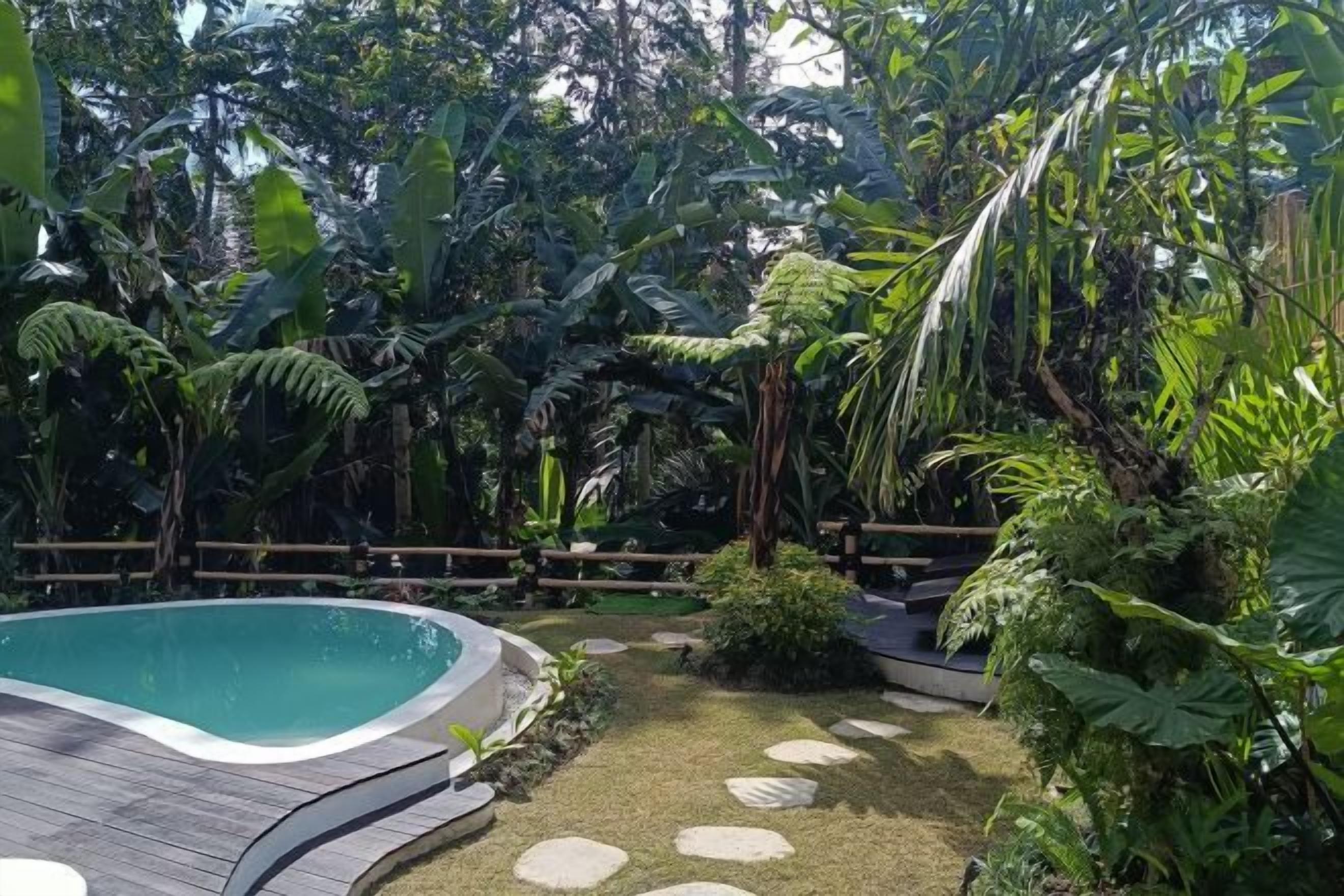 A pool surrounded by tropical vegetation and a wooden deck.