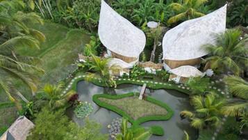 A tropical resort with two large white structures surrounded by lush greenery and a central pond.