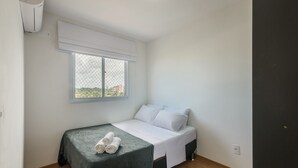 Una habitación pequeña y limpia con cama, ventana y aire acondicionado.