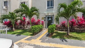 Un edificio residencial con entrada protegida por una reja, rodeado de abundante vegetación y palmeras.