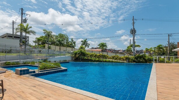 Una piscina con muelle de madera, rodeada de palmeras y vista a un paisaje urbano.