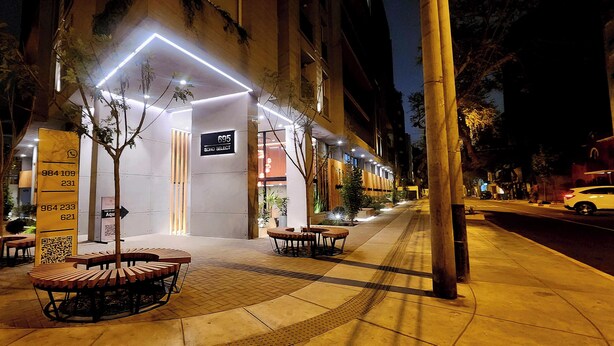 A hotel entrance with a modern design, featuring a reception desk, a signboard, and a seating area with tables and chairs. - Luxury Stay Miraflores | Entre Marriott & Pullman (Miraflores)