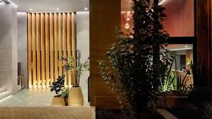 A modern lobby with a vertical wooden panel wall, potted plants, and a reception desk. - Luxury Stay Miraflores | Entre Marriott & Pullman (Miraflores)