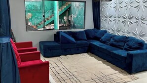 A modern living room with a sectional sofa, a red chair, a large window with a view of a staircase, and a decorative wall panel. - House in Cumbuco  (Caucaia)