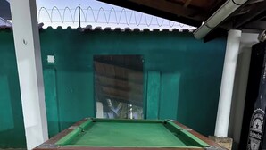 Une table de billard recouverte d’un drap vert, entourée d’un mur vert et d’une bouteille de bière Heineken.